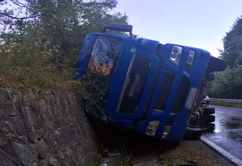 FOTO: TIR plin cu bușteni, răsturnat într-o curbă periculoasă, pe DN 17C, la ieșire din Năsăud